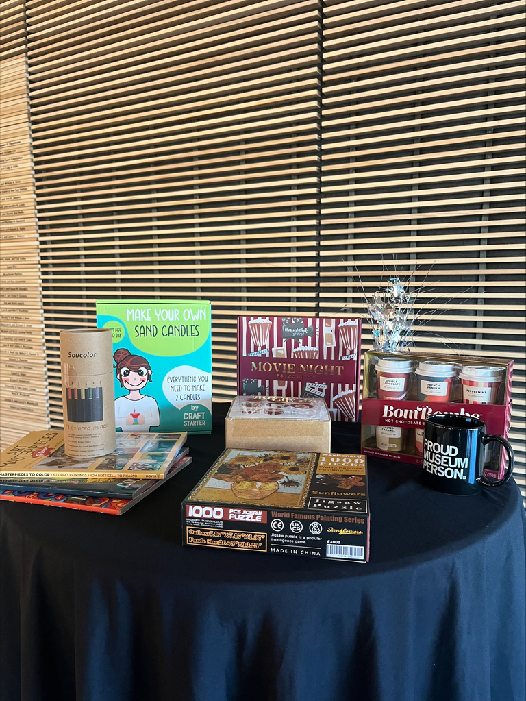 round cocktail table with an assortment of prizes. These include a candle making kit, coloring book with pencils, popcorn kit, and a hot chocolate kit with a mug 
