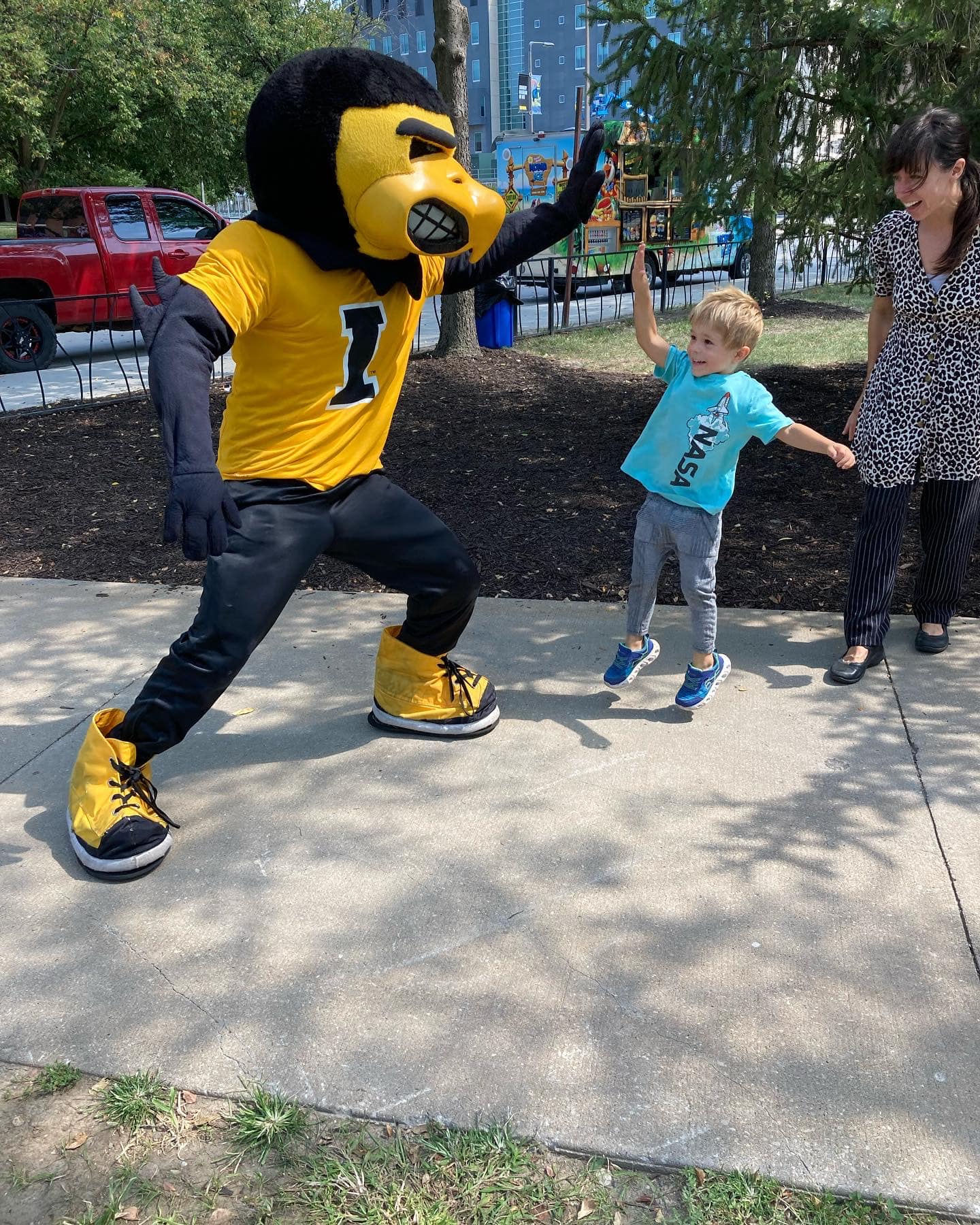 A small boy in a light blue shirt jumps in the air to give University of Iowa mascot Herky a high five.