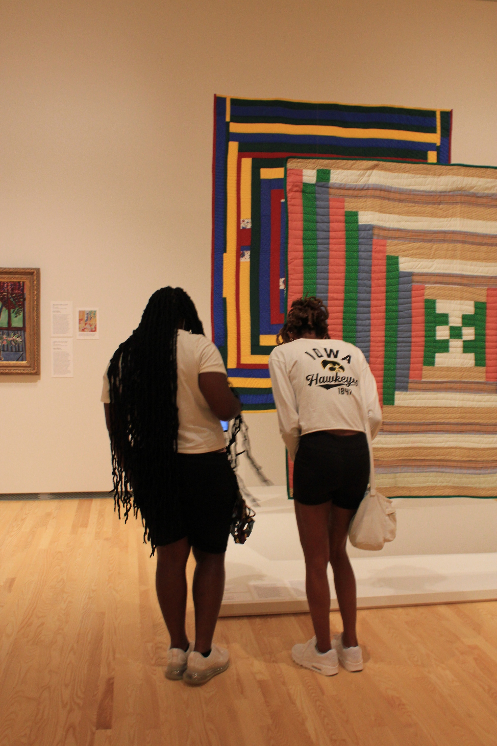 Two women with dark hair stand in front of brightly colored quilts hanging in a museum gallery