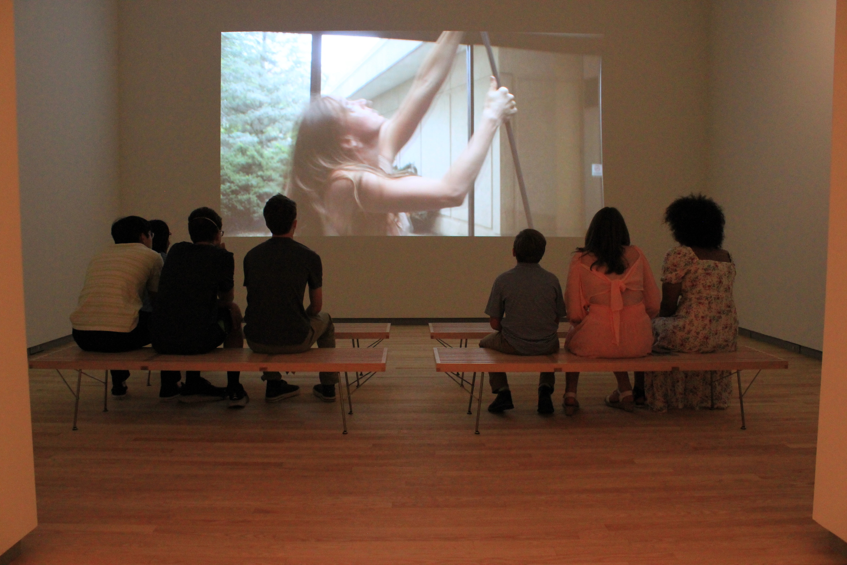 People seated on two benches watch a video in a darkened room