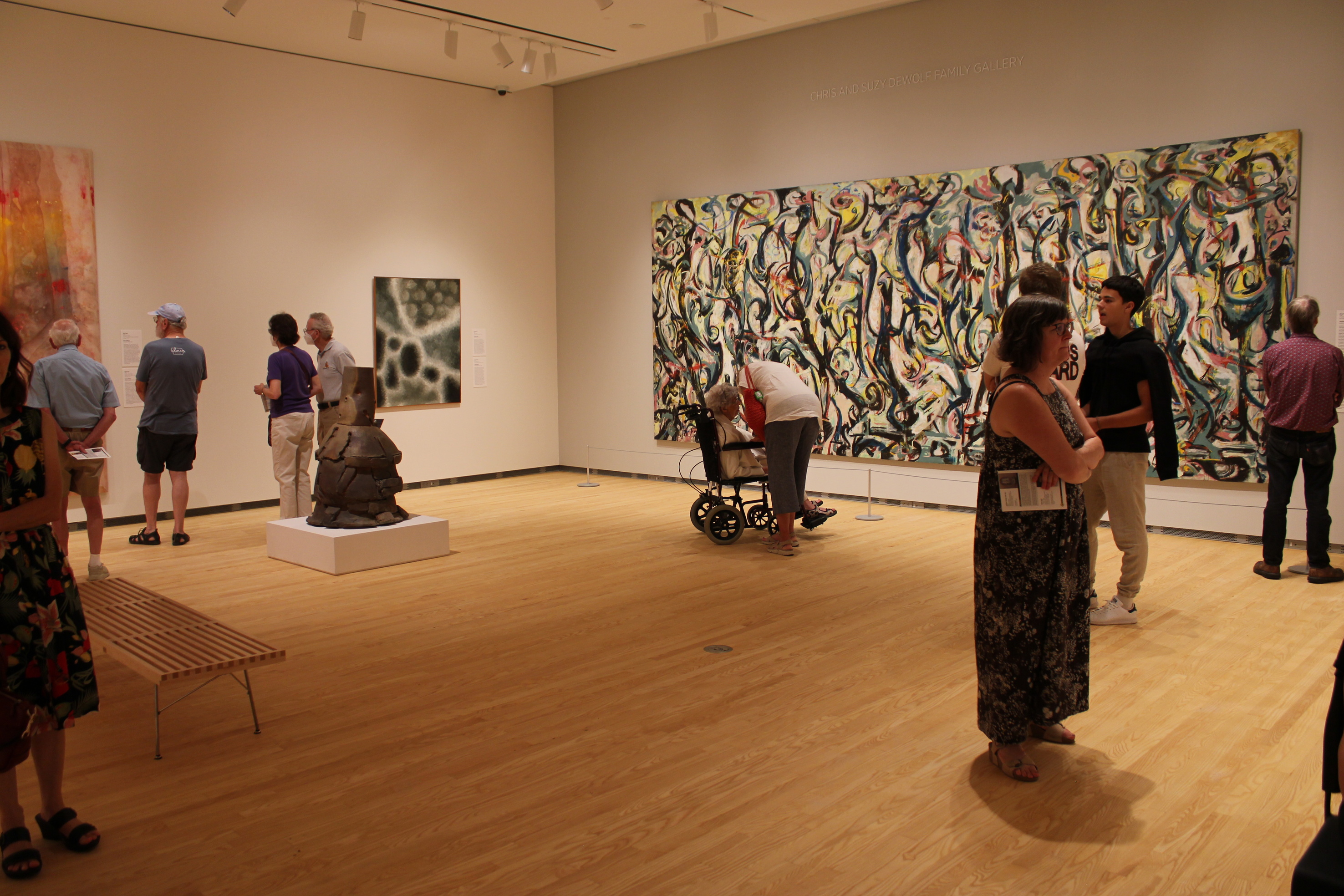 Visitors in a museum gallery look at paintings and a large ceramic sculpture