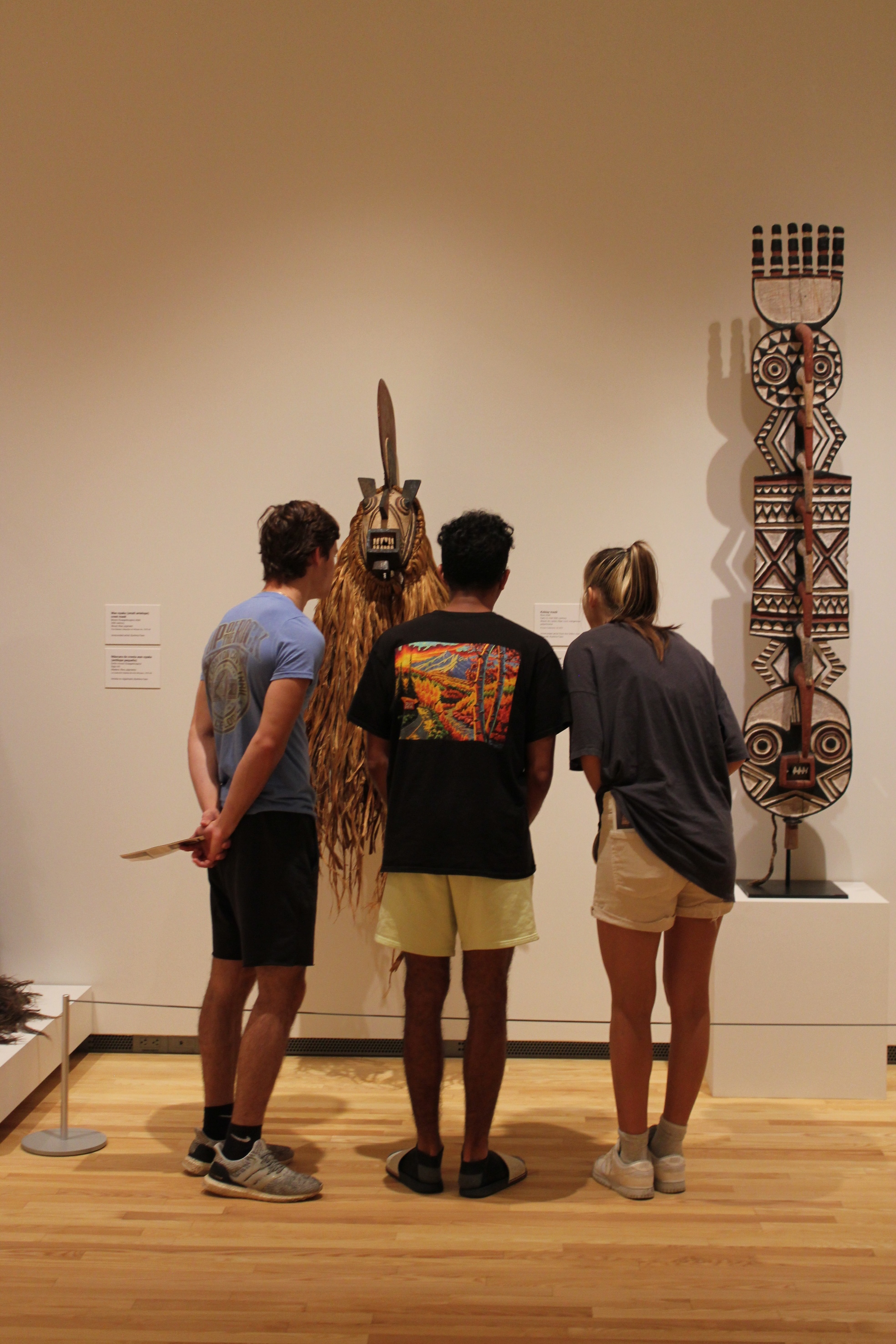 A group of three university students look at a large African mask