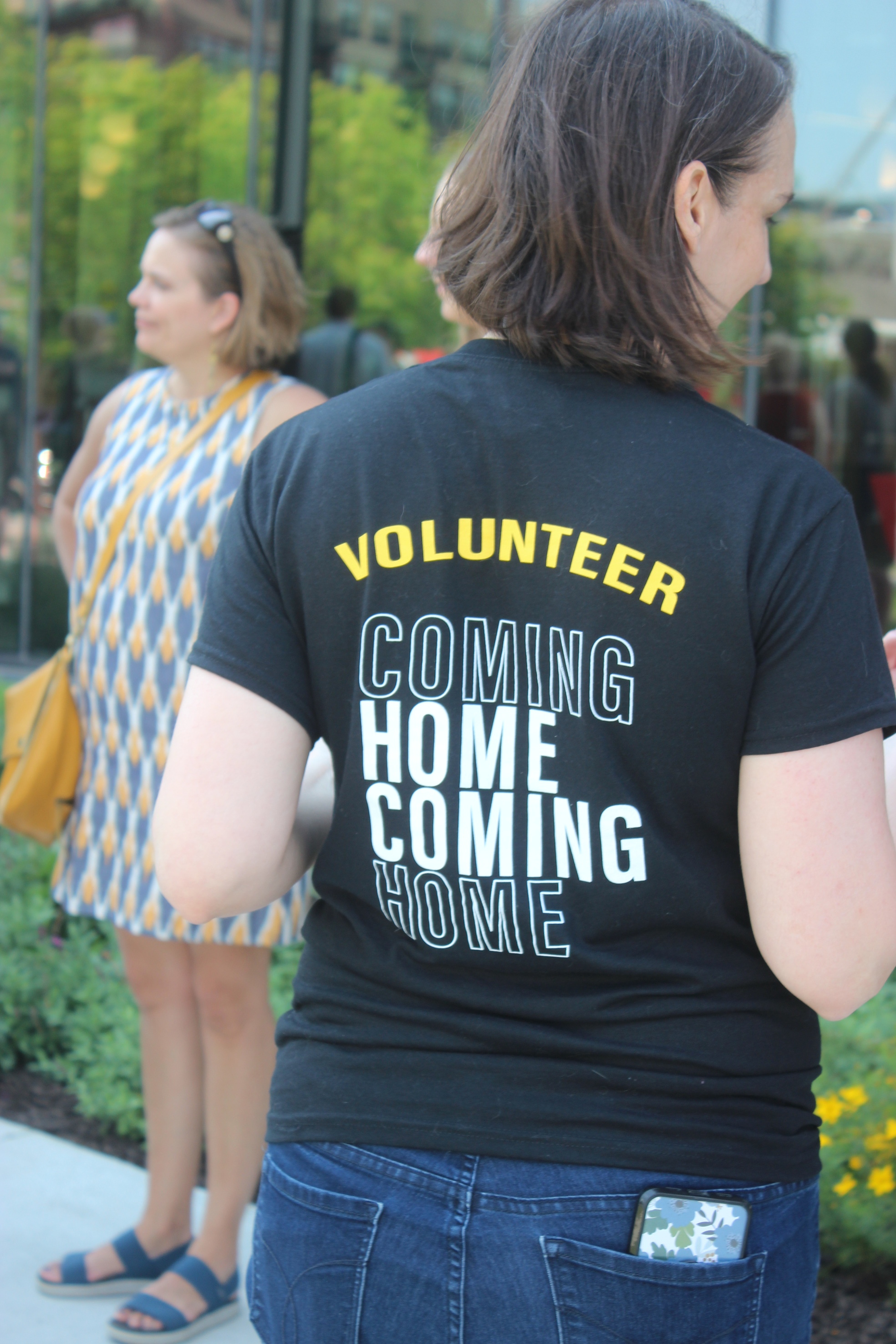 Woman with short dark hair seen from behind. She wears a t-shirt that reads "Volunteer.  Homecoming"