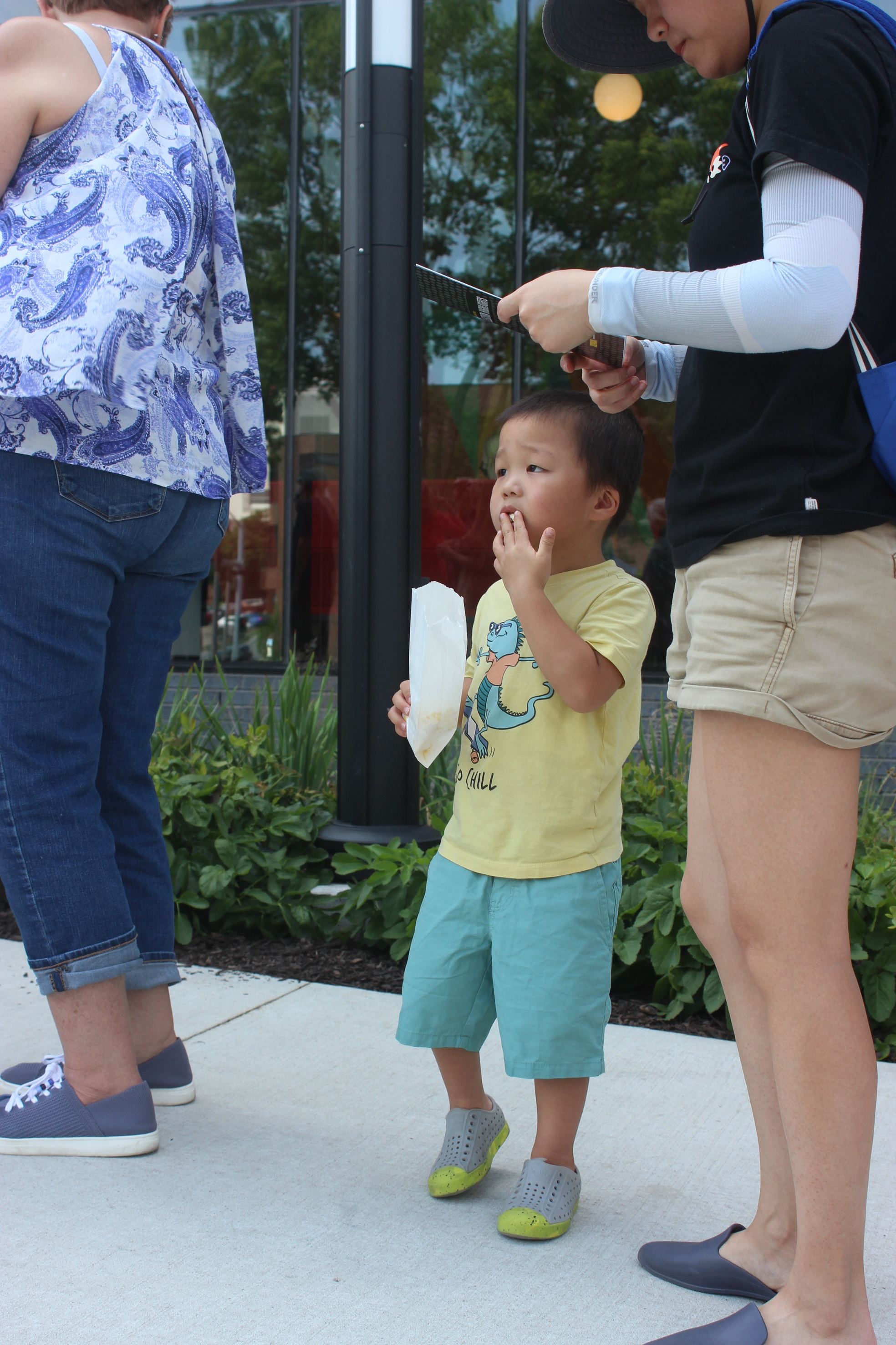 Small child wearing a yellow t-shirt and green shorts eats popcorn out of a bag