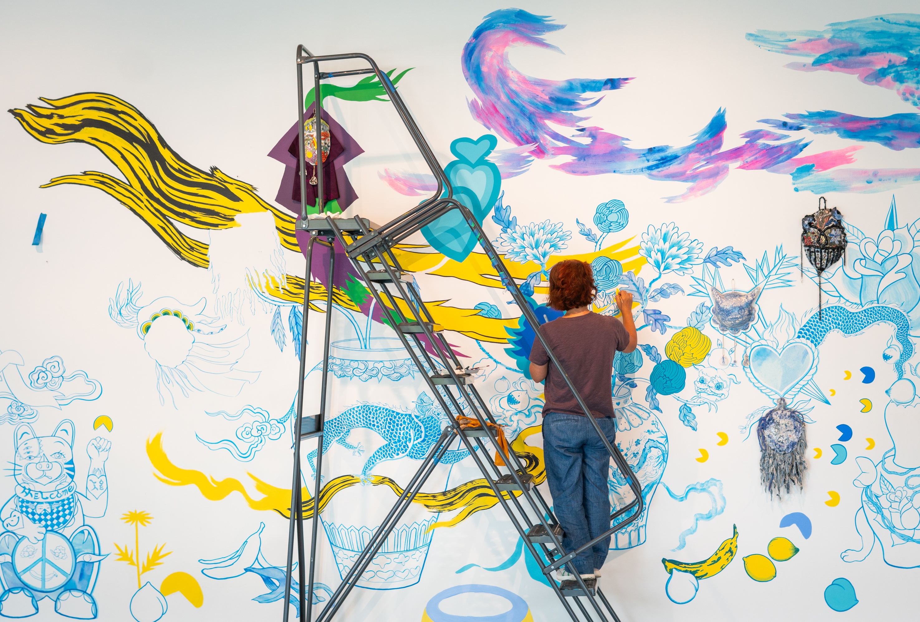 A person on a ladder painting vibrant designs on a wall