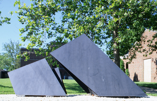 Two steel, pyramid-like structures emerging from the ground. The larger of the two leans towards the smaller.