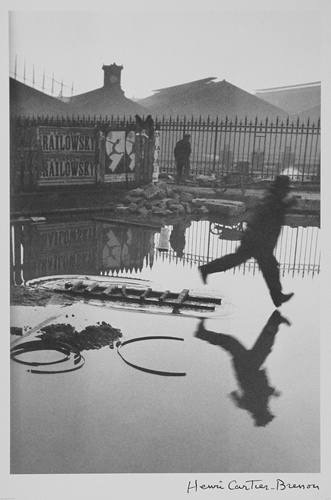 black and white photograph of a man leaping across a wide puddle