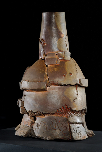 Abstract, vaguely bottle shaped sculpture with asymmetrical stacks of clay, and cracks and fissures that make visible the process of sculpting and firing.