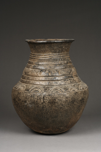 Large earthenware pot with a stout base and sides that angle slighly inward as they reach the top then flare out again creating a rim around the opening.