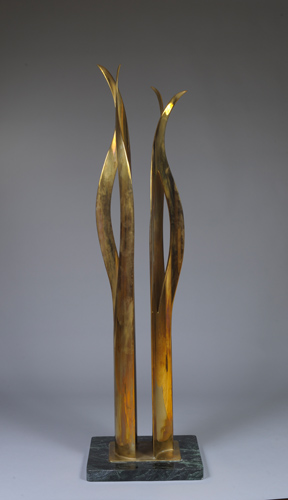 A bronze sculpture composed of two grass-like pieces that reach upward. The pieces each split towards the middle, bow apart, and come back together at the top, with the tips reaching away.