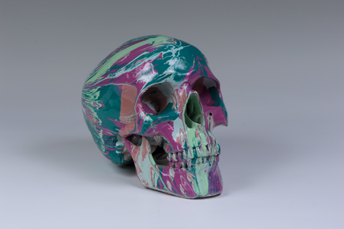 A human skull covered in swirling green and pink hues.