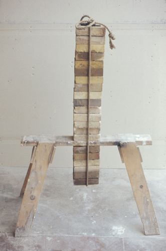 A wooden sawhorse with a column of bricks tied above and below.