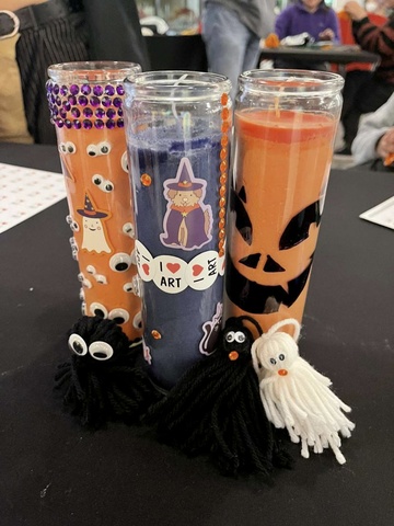 Another example of the event's crafts: Three votive candles (two orange and one purple) decorated with stickers, rhinestones, and markers, and then several pompom creatures with google eyes and other embellishments.