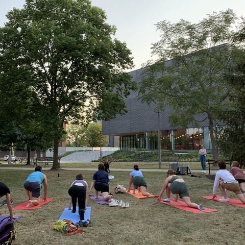 Students doing yoga in Gibson Square Park. The photo is taken from behind, with the Stanley Museum of Art visible in the background.