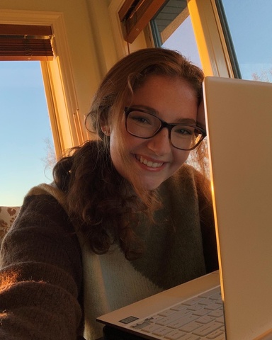 A photo of Emalie Brannigan: she is posing, half hidden by her laptop screen, smiling down at the camera.