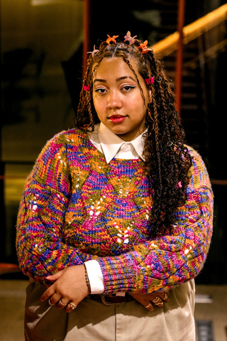 A photo of Lily Hester: they are posing in Art Building West, wearing a very colorful sweater.