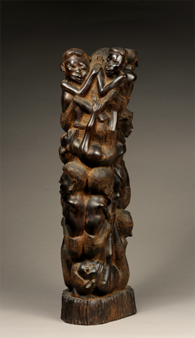 A photo of an artwork, carved from a single upright piece of wood and burnished to a shiny dark brown surface, featuring the carvings of small human figures climbing a central column.