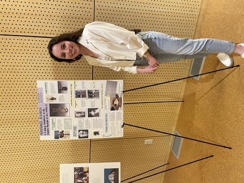 A photo of Monica standing beside a poster she made at the Iowa Arts Fest, detailing her work as part of Cory Gundlach's class.