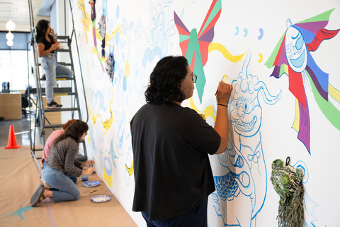 A photo of Stanley student employee, Shaun Mallonga, working on Jiha Moon's mural, 'One An Other,' in the Stanley Museum of Art lobby.