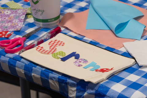 A close up view of a student's patchwork project: the name "Sarena" patchworked onto a white canvas pencil case, each letter of the name cut out of a different patterned piece of fabric.