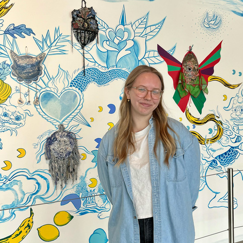 A photo of Josie, posing in front of the Jiha Moon mural in the Stanley lobby.