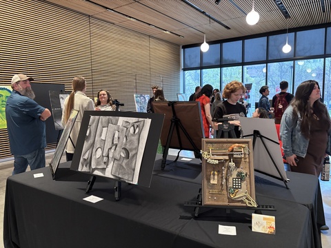 A group of people explore artworks on display at the 2025 Student Exhibit.