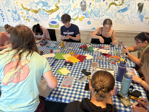 Students sit around a table, carving linoleum blocks to make stamps.