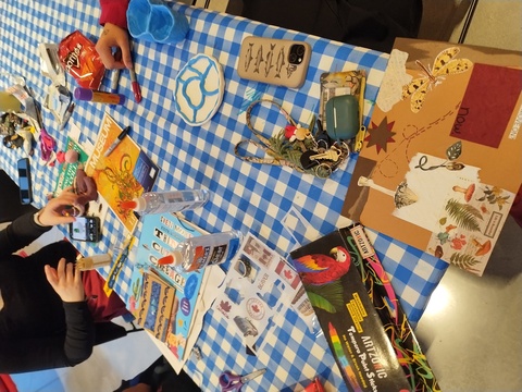 A top-down view of a table with a blue and white checkered tablecloth with art supplies scattered over it. 