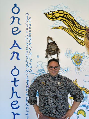 Shaun poses, hands on their hips, in front of the Jiha Moon mural in the museum lobby, underneath where their name ("Shaun Peter") is painted on the wall.