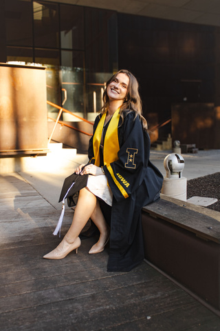 Amelia poses in her graduation cap and gown outside of Art Building West.