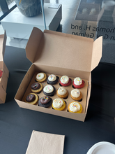 A photo of the cupcakes at the HBD SMA event. There are 12 of them in a cardboard box, with different colored cakes and frosting.