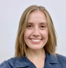 A headshot photo of a smiling blonde woman in a blue collared top.