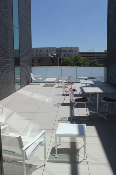 A narrow terrace with white chairs and tables overlooks surrounding buildings.