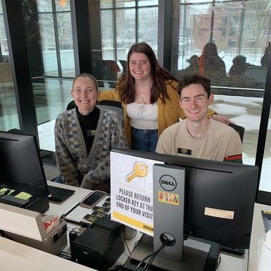 A photo of three gallery hosts at the Stanley's front desk; two are seated, with the third standing behind them. 