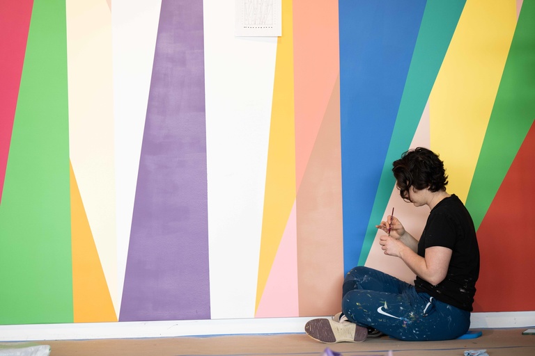 Jenna Pirello, seated on the floor, applies paint during the installation of "Surrounding."
