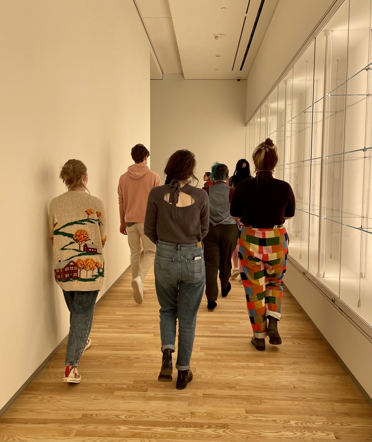 A group of students, seen from the back, walk through a Stanley Museum of Art gallery