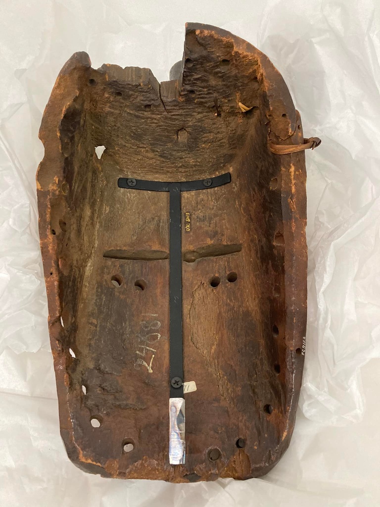 Interior of a wooden face mask with t-shaped metal bracket attached to the surface.