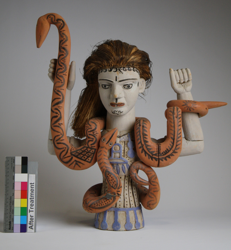 Front view of Mami Wata figure. The bust of a woman with long hair and a snake wrapped around her upraised arms.