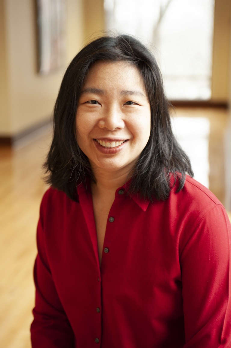 Woman with shoulder-length black hair wearing a red, long-sleeved shirt looks at viewer