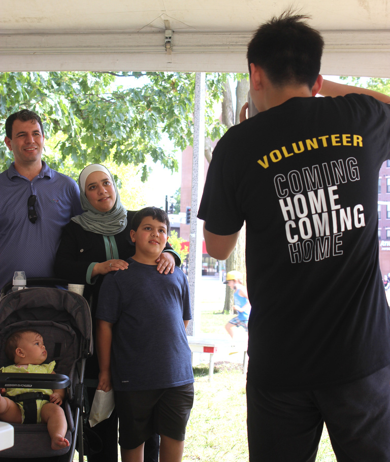 A man wearing a black t-shirt that reads "Volunteer" takes a photo of a family