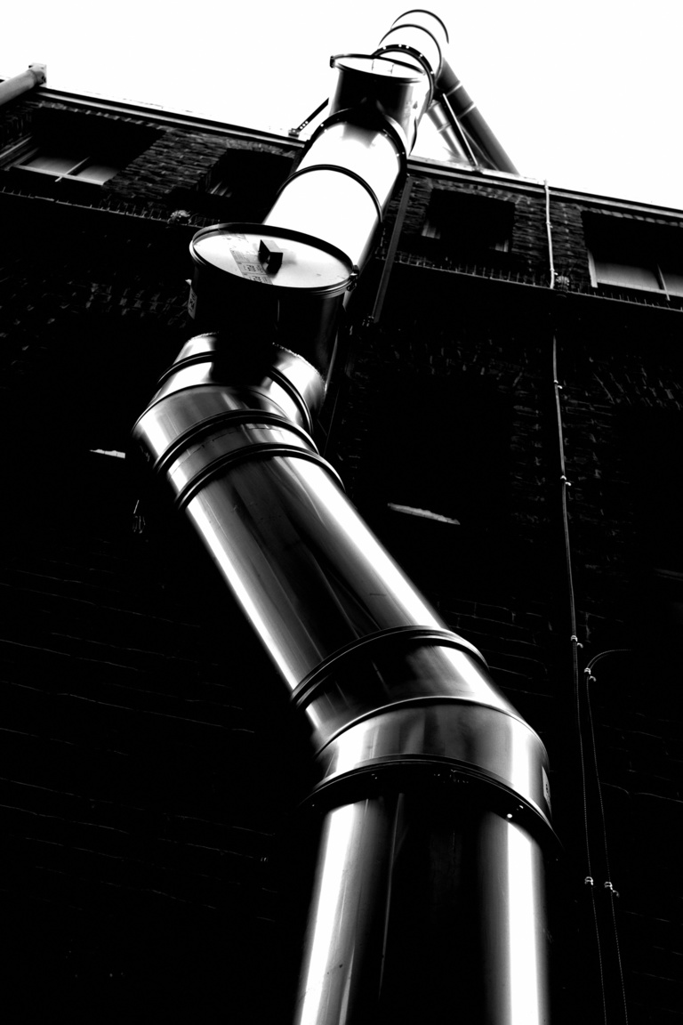 Graham's art: a black and white highly contrasted photo of a pipe climbing a wall.