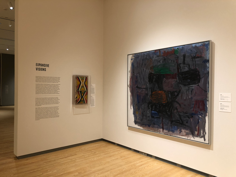 An installation shot of the galleries at the Stanley Museum of Art. A work by Phillip Guston is visible, alongside a parfleche, and the text for the "Expansive Visions" section of the exhibition.