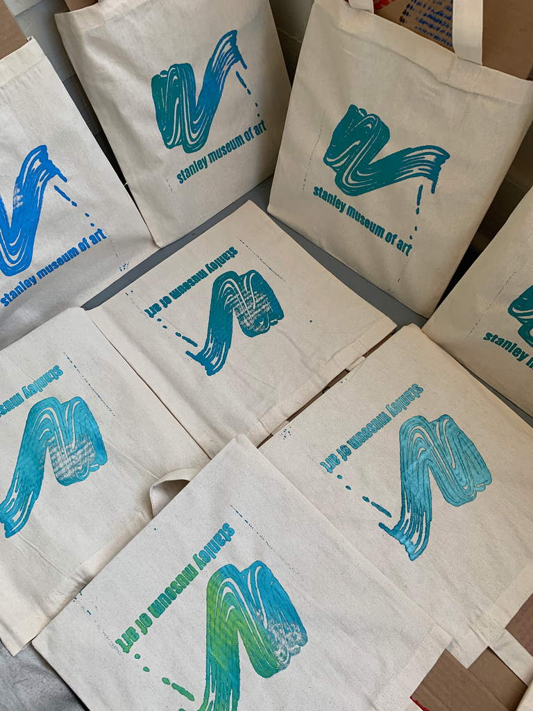 Eight tote bags fill the photograph--they are laid out along the floor to dry, all in different but similar shades and mixes of blue, green, and turquoise.