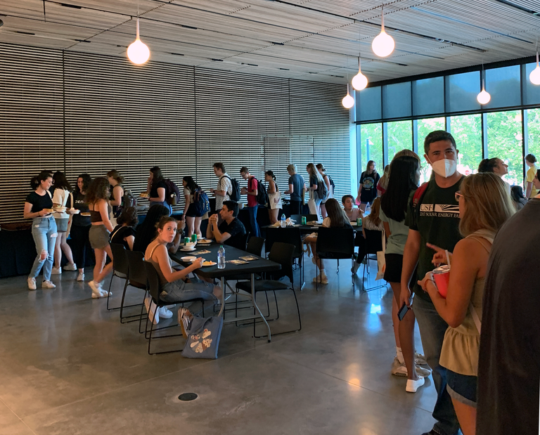 An interior shot of the Stanley Museum of Art lobby. The lobby is filled with students; some are waiting in a long, winding line to grab food, while others are seated at tables eating and chatting.