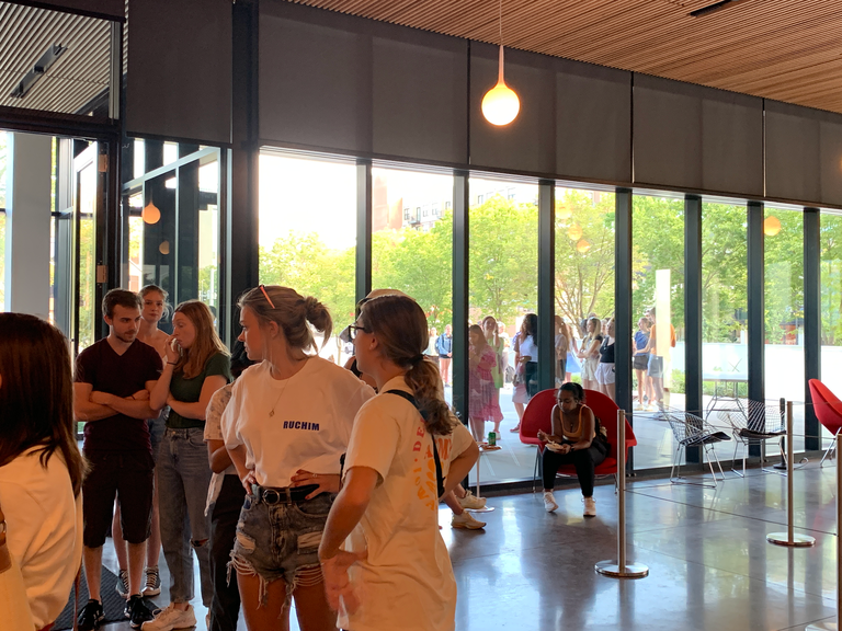 A view from inside the Stanley Museum of Art lobby showing a line out the front door of students waiting to get inside to grab a tote bag or a slice of pizza.