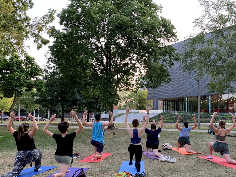 Students doing yoga in Gibson Square Park. The photo is taken from behind, with the Stanley Museum of Art visible in the background.