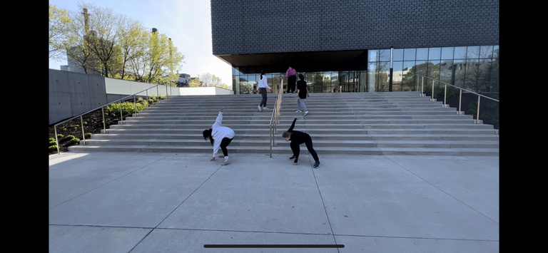 A still image from a video of a dance project choreographed by Katherine Shamdin. In it, 5 students dance on the front steps of the Stanley.