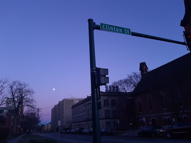 A photo of the sky looking up at a street sign, with a tiny moon visible.