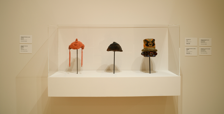 An installation shot, featuring three pieces of headwear in a glass case.
