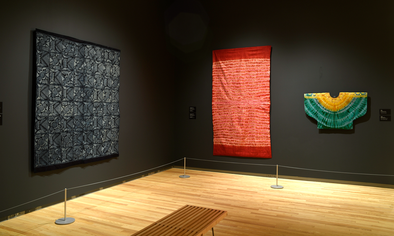 An installation shot of "Centering on Cloth" featuring two large textiles and a smaller garment.